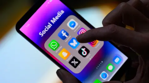 Getty Images A silhouetted image of a hand scrolling a smartphone, with social media apps featured on the screen