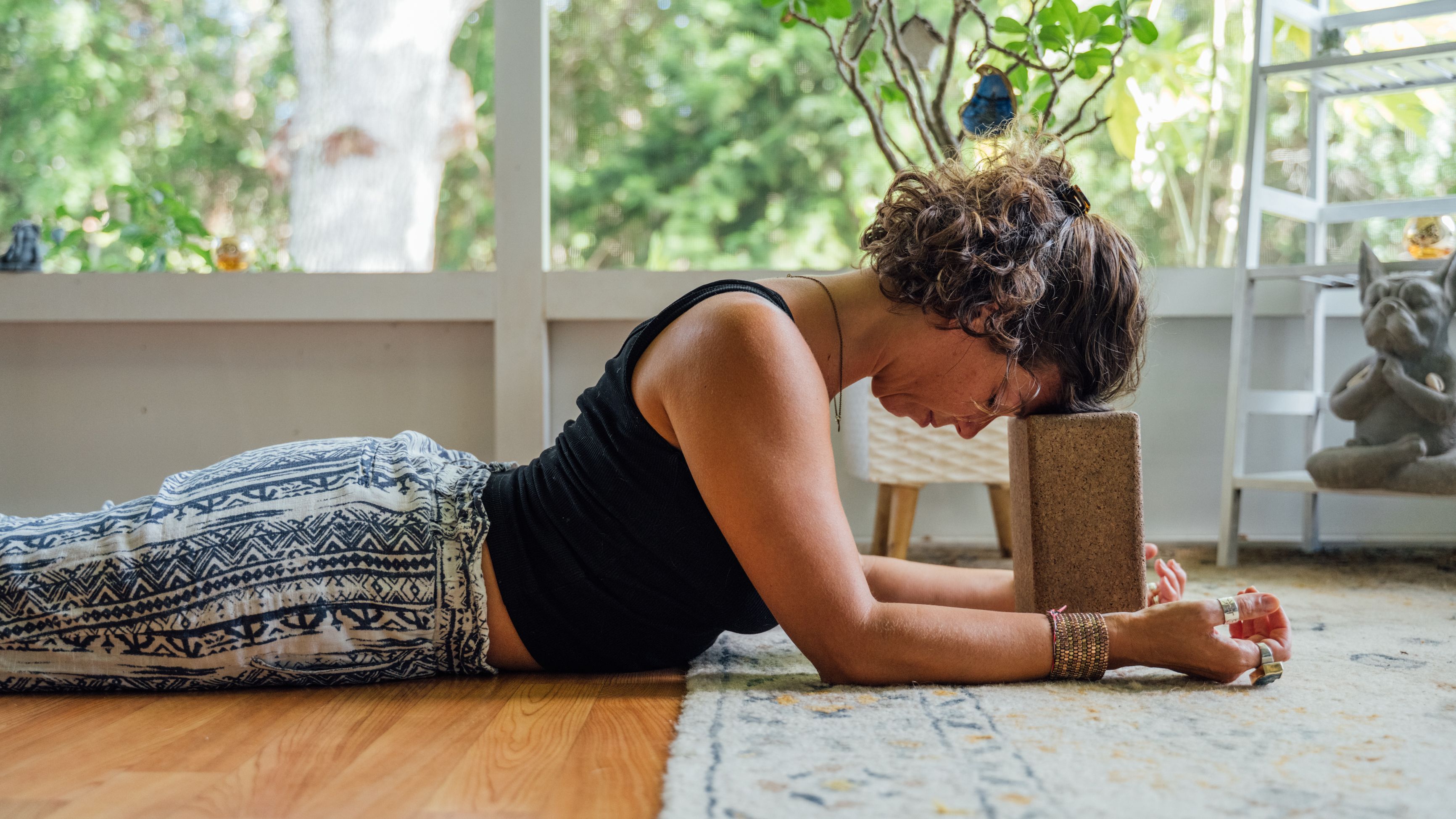 Woman lies on her front on the floor with her forehead resting on a yoga block