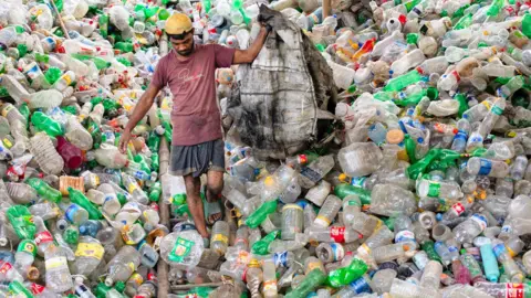 Getty Images A man walks down a massive pile of plastic bottles in Bangladesh
