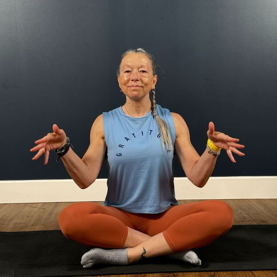 Woman sits cross-legged on mat demonstrating wrist movement