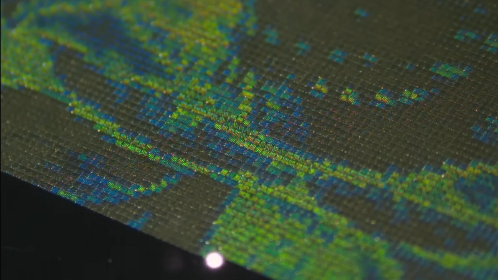 An array of tiny parallel green lines appears over a steel surface. The white dot a laser beam is visible in the lower center of the picture.
