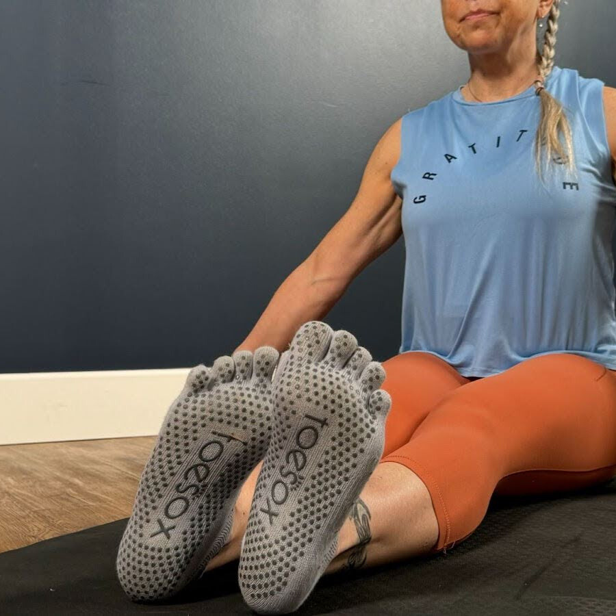 Woman sits cross-legged on mat demonstrating wrist movement