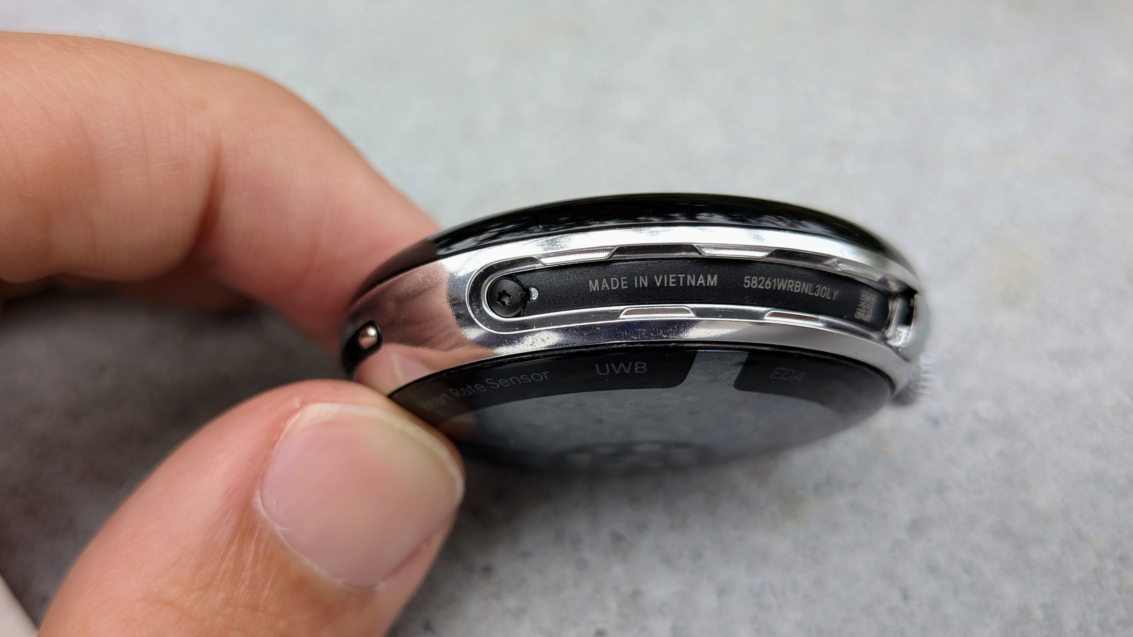 A photo of the Google Pixel Watch 4 45mm case held in hand, with the bands removed, exposing a slot where a screw is visible.