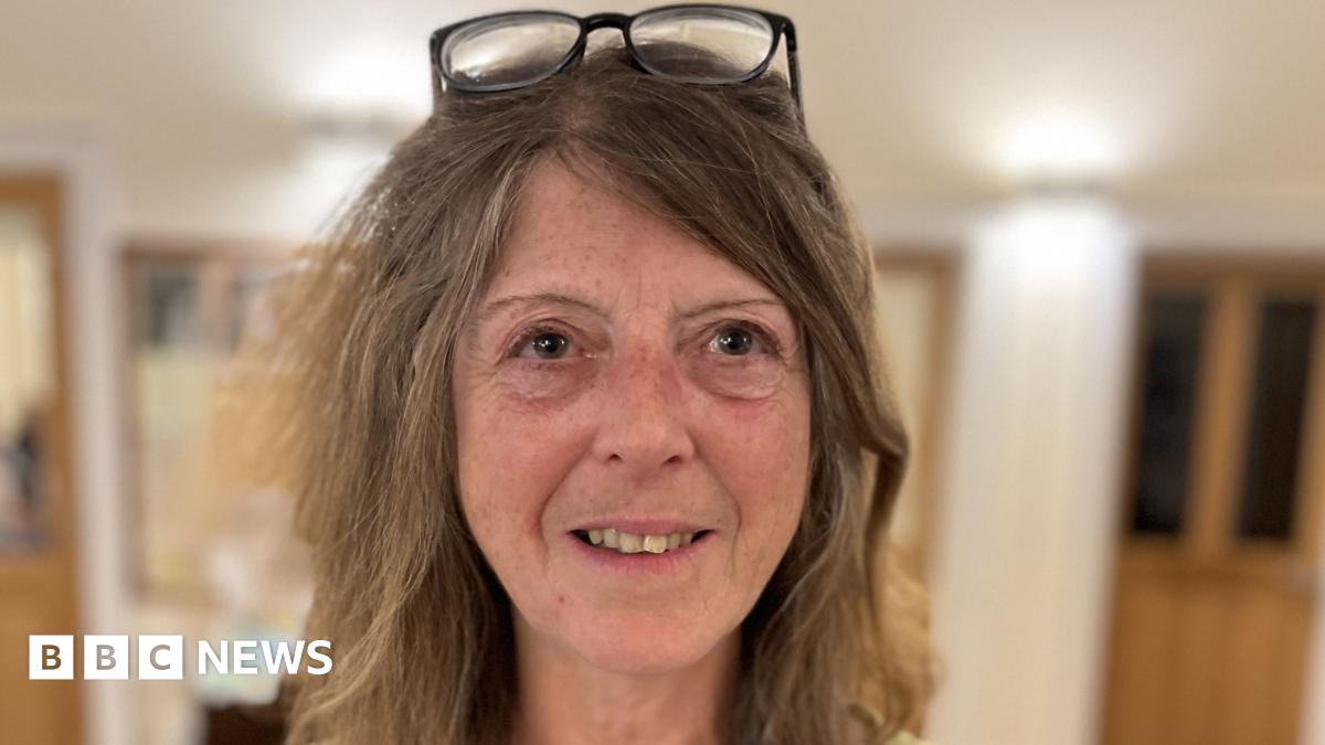 Di Cross with light brown shoulder length hair smiling with glasses on her head
