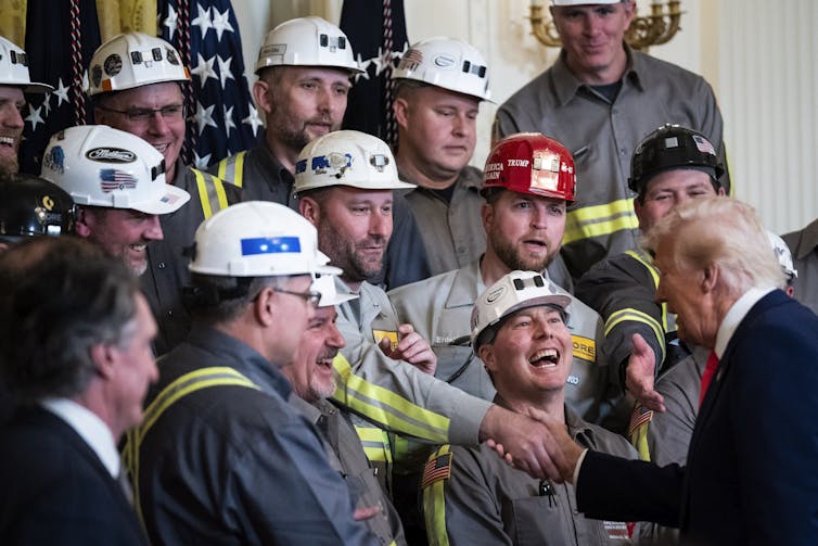 Trump shakes a man's hand. All of the men are wearing hardhats.