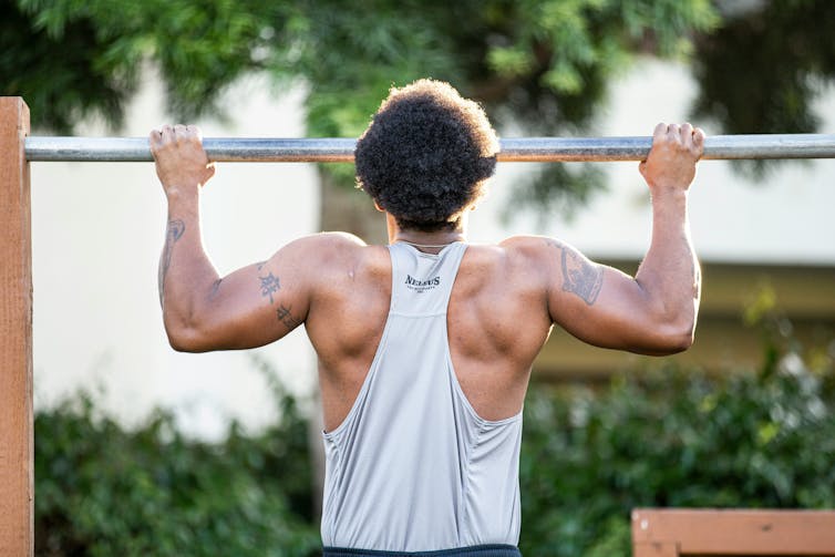 A man attempts a chin-up on a metal bar in a park outside