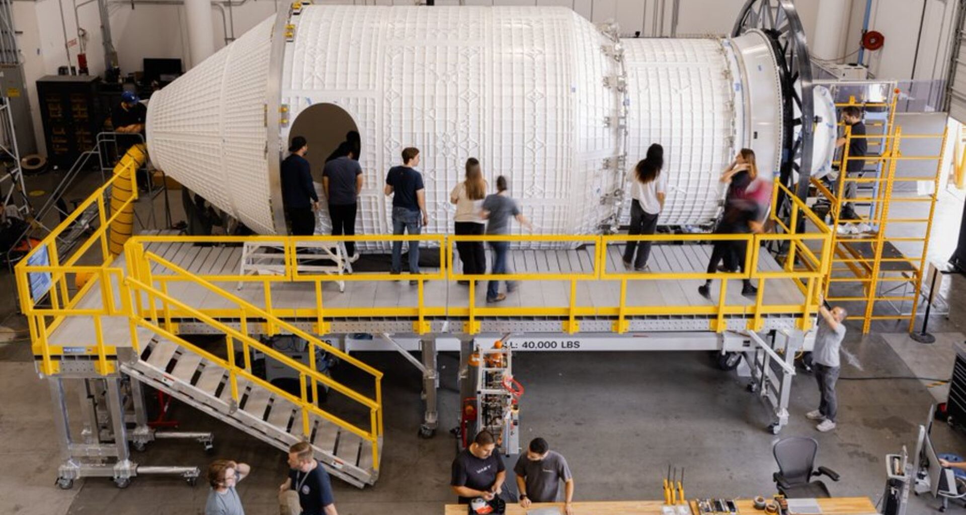 A series of people stand around a large space station in a giant warehouse