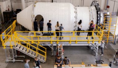 A series of people stand around a large space station in a giant warehouse