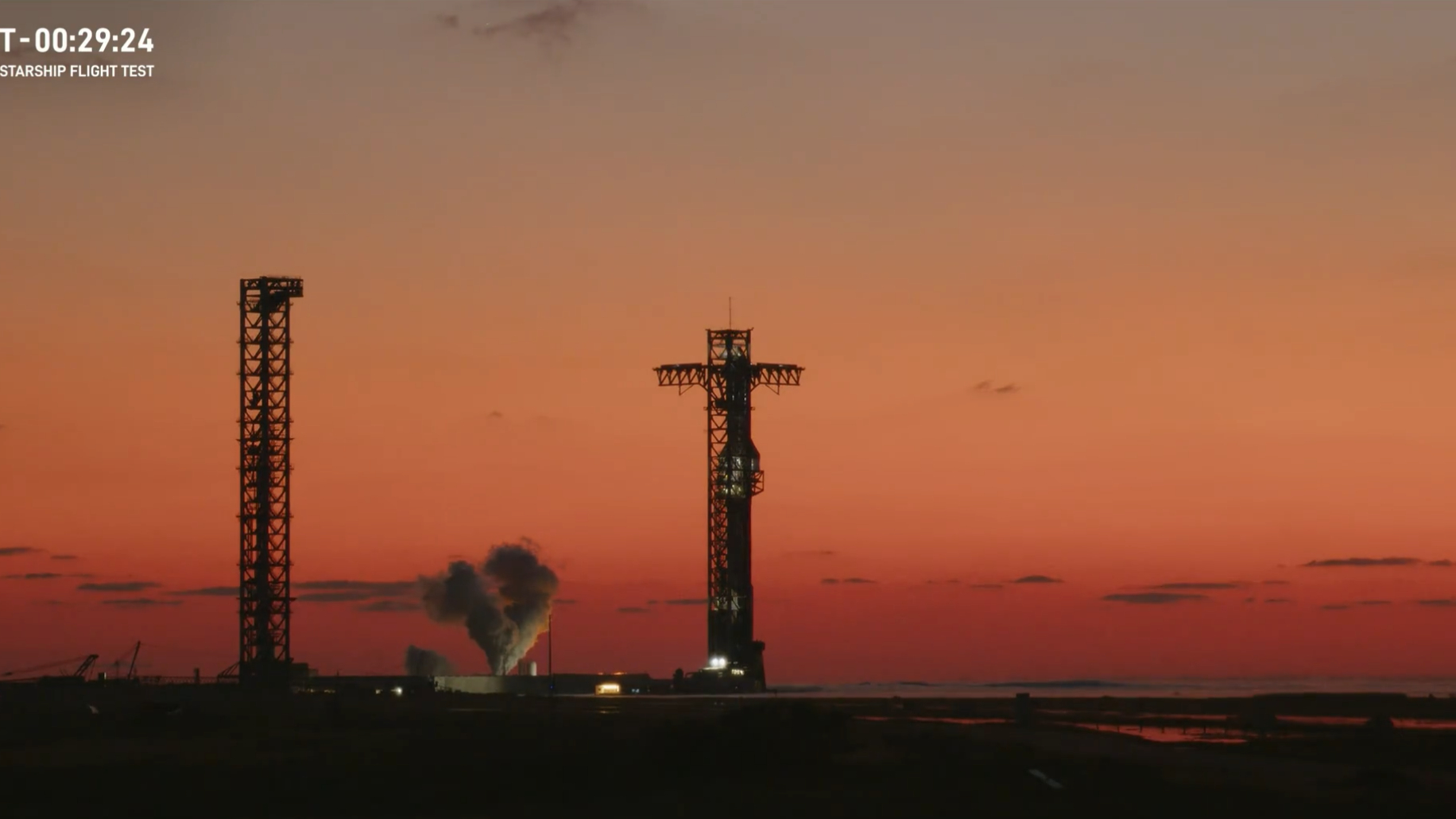 A giant SpaceX Starship rocket on the launch pad just before sunrise with a plume of gas