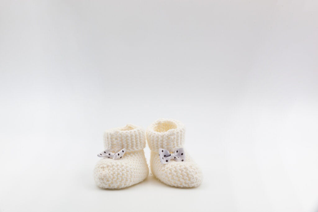 Knitted white baby booties with polka-dot bows on a gray isolated background.