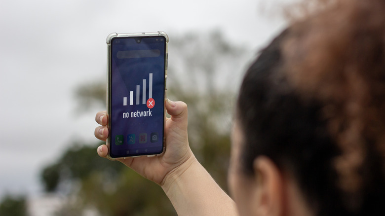 A person holds up a smartphone with no signal