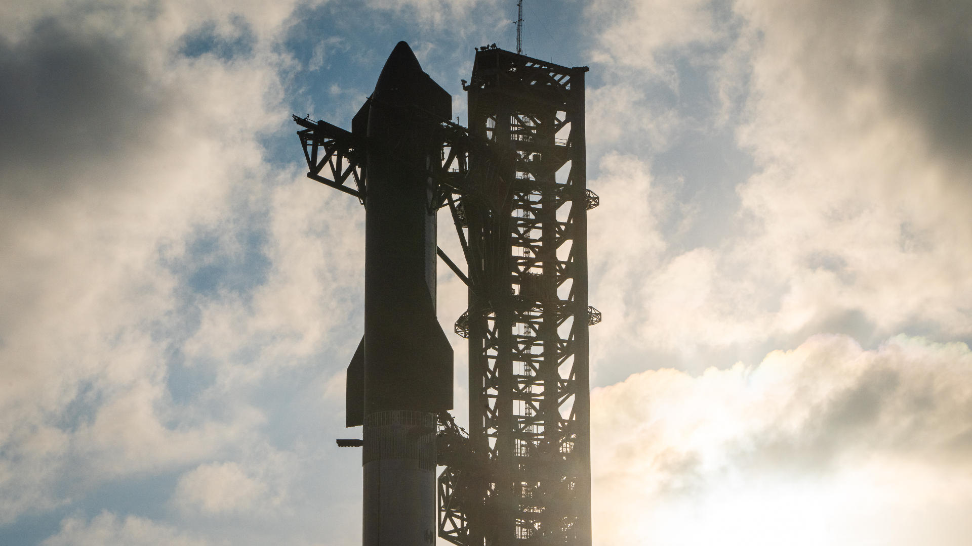 A SpaceX Starship rocket atop its booster at launchpad with clouds overhead