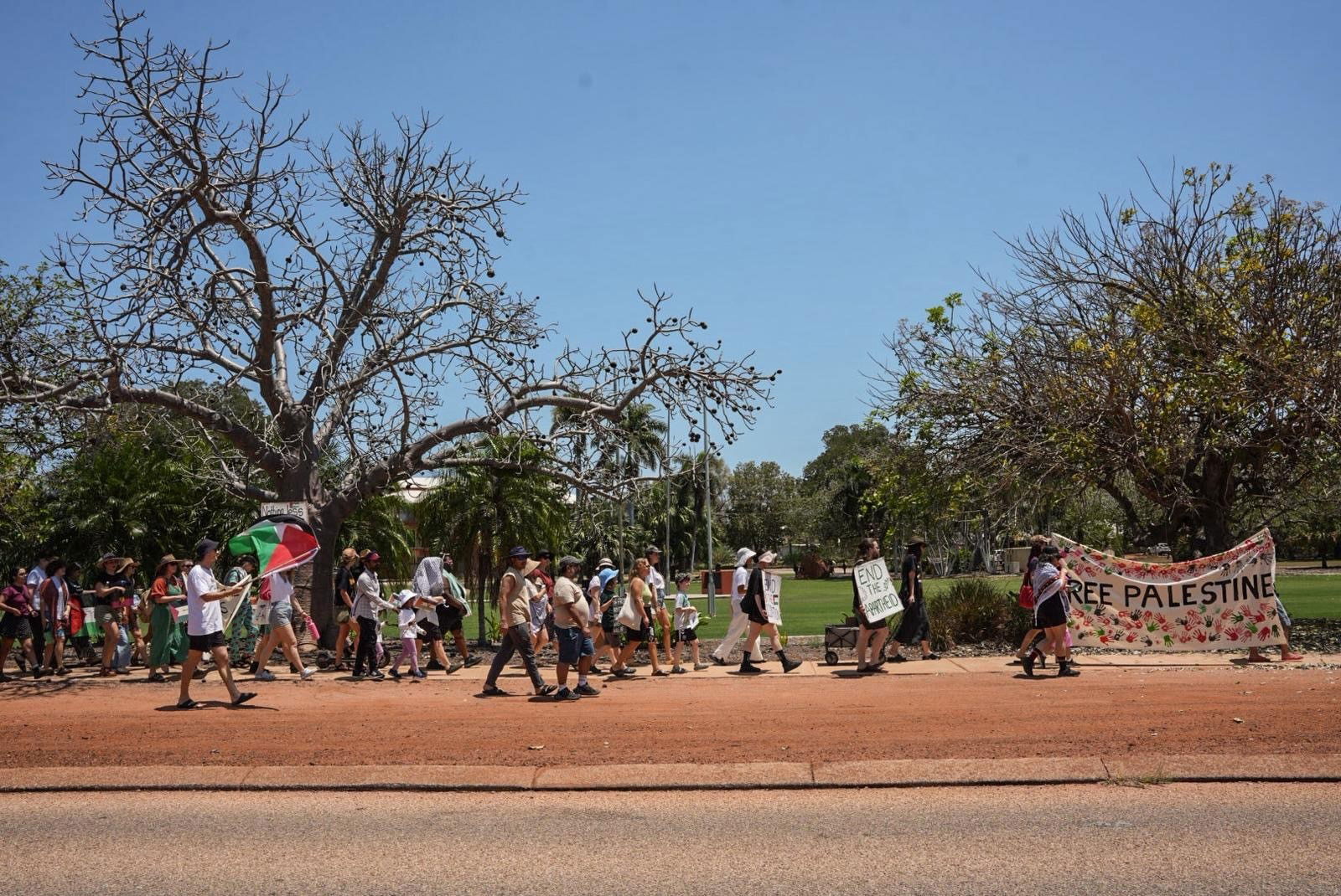 A crowd of protesters walk along red dirt