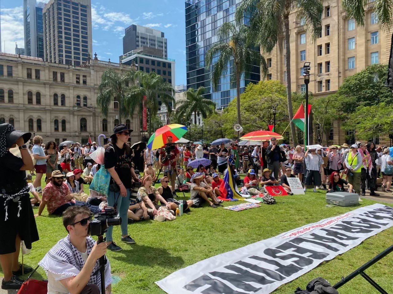 Crowds gathered on the lawn with Palestinian flags, rainbow umbrellas