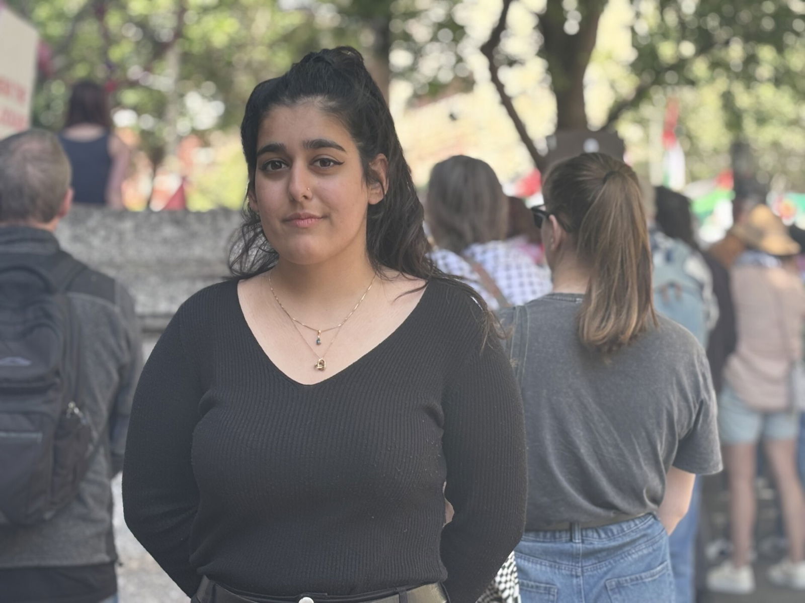 A woman in a black long-sleeved shirt stands with her hands behind her back