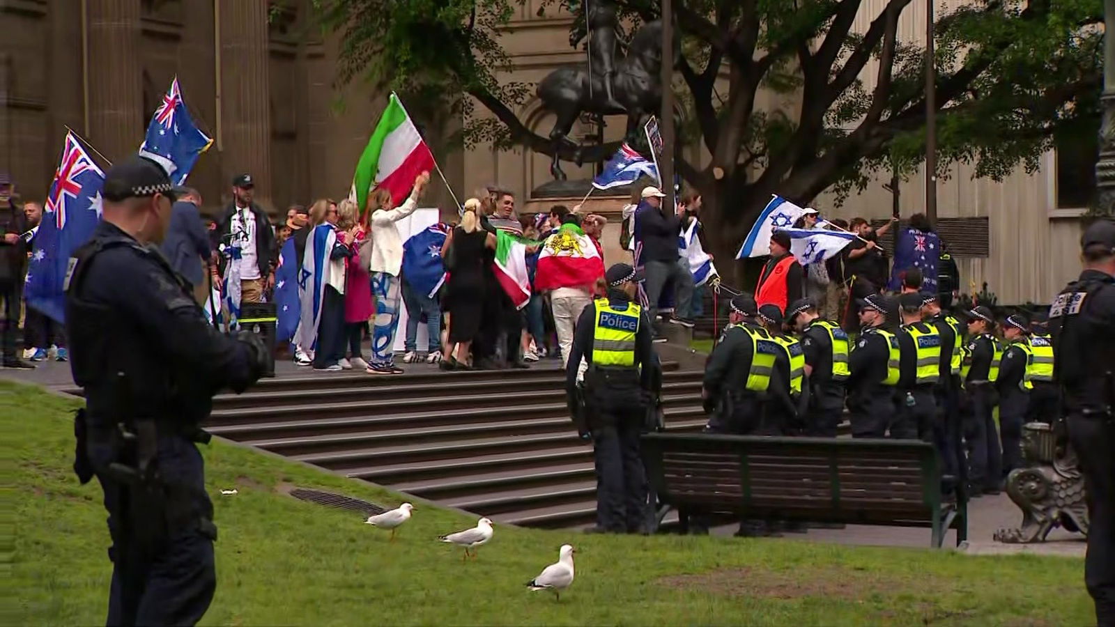A line of police watch a crowd of protesters with Australian and Israeli flags