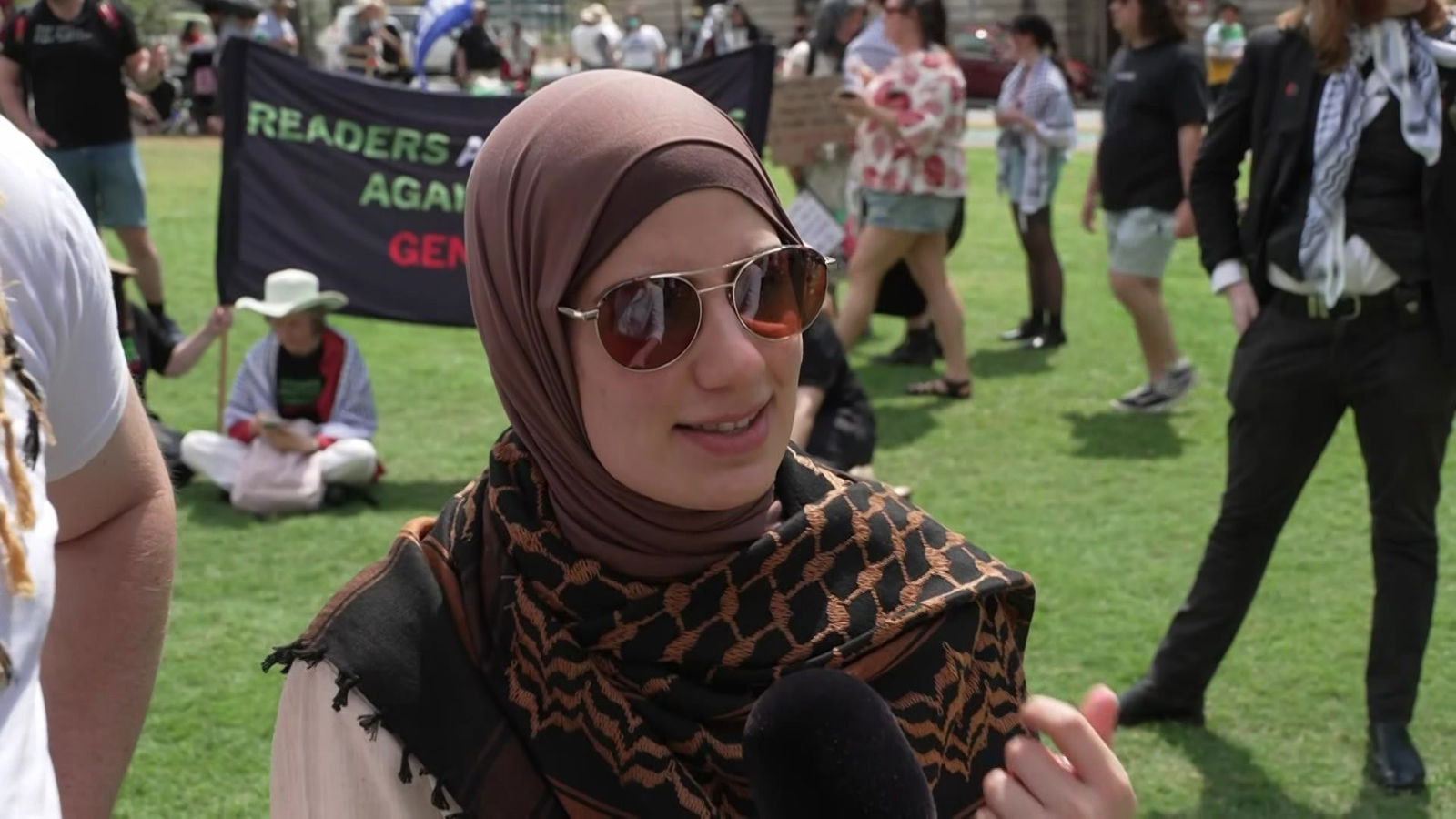 Woman in headdress and sunglasses speaks into microphone
