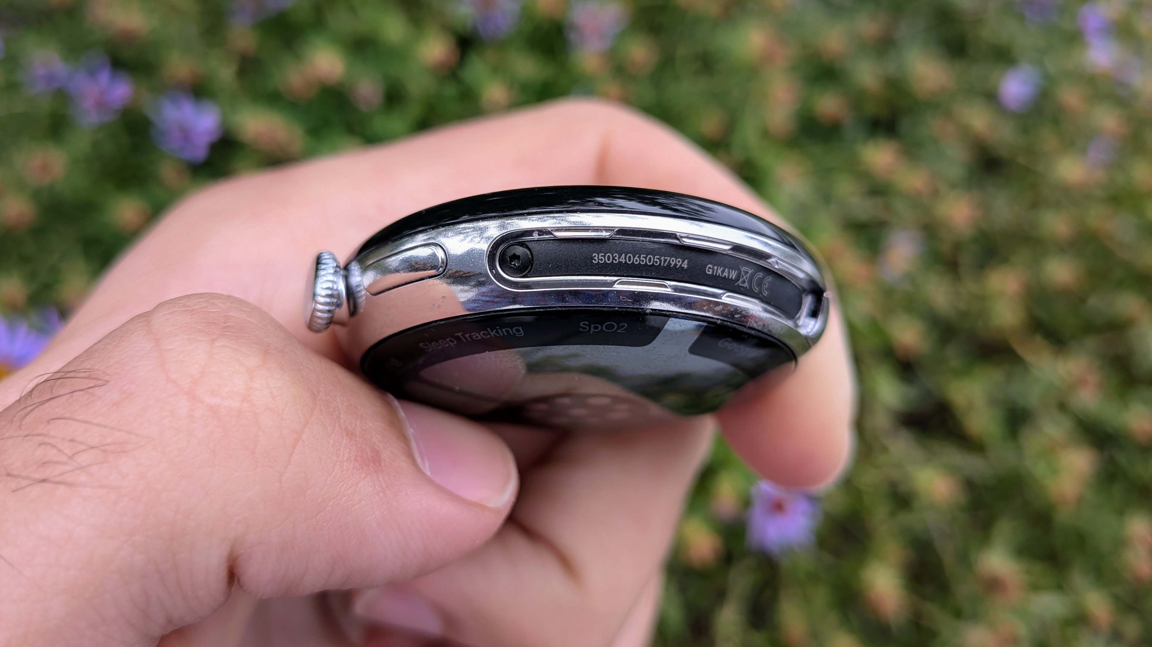 A photo of the Google Pixel Watch 4 45mm case held in hand, with the bands removed, exposing a slot where a screw is visible.