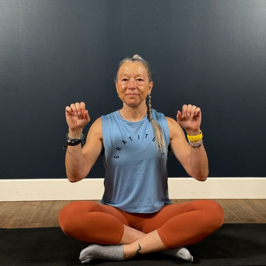 Woman sits cross-legged on mat demonstrating wrist movement