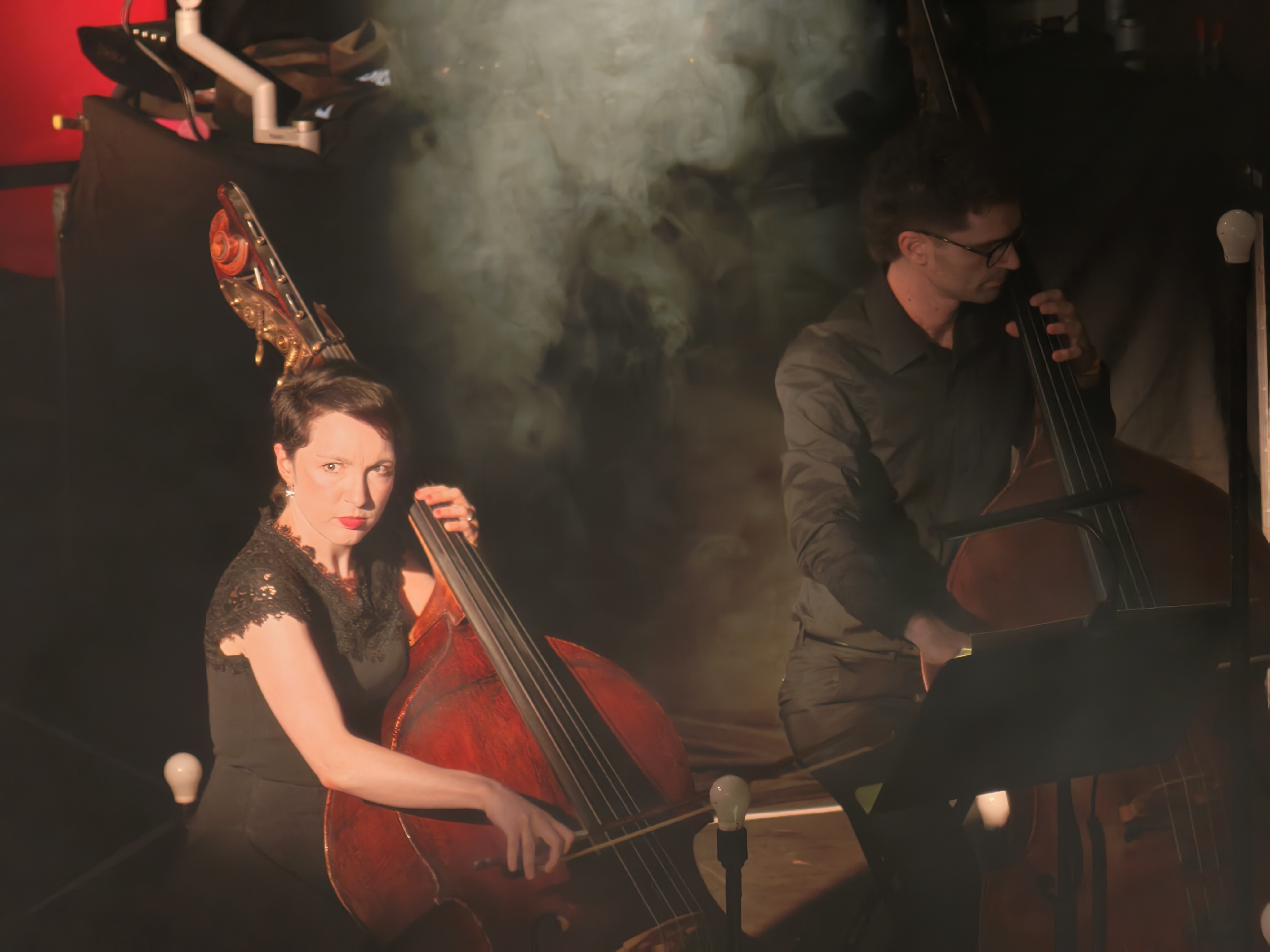Two cellists playing music in a dark and smoky stage