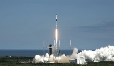 A white and black rocket lifts off against a blue sky.