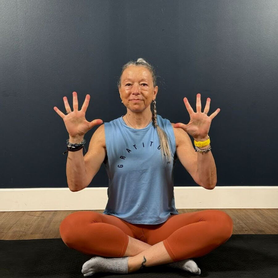 Woman sits cross-legged on mat demonstrating wrist movement