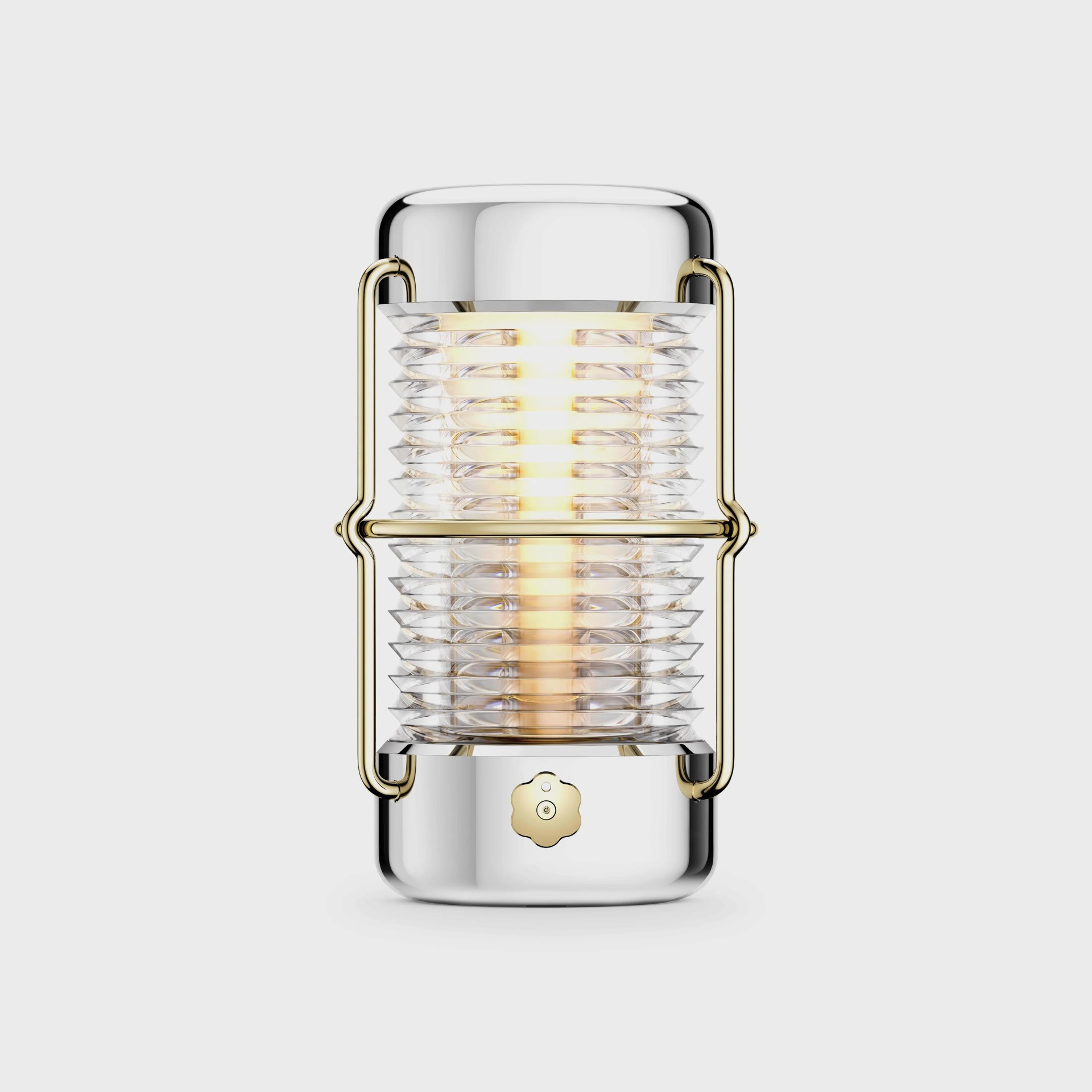 A modern, cylindrical lantern-style light with a polished silver body and gold accents. The central light source is surrounded by a clear, ribbed glass diffuser, held in place by a gold metal frame. The light emits a warm glow, and there is a small, flower-shaped gold knob at the bottom front of the lantern. The background is plain and light gray.