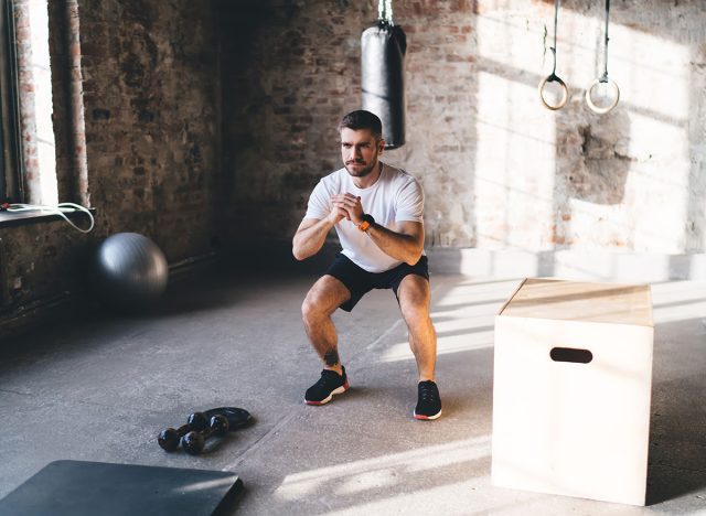 Full body of strong male athlete doing squats while training muscles stretching legs standing in chair pose during workout at gym