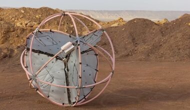 Tumbleweed rovers: spherical object composed of interlocking loops, with rounded flat panels inside it. It is sitting near mounds of dirt in a desert.
