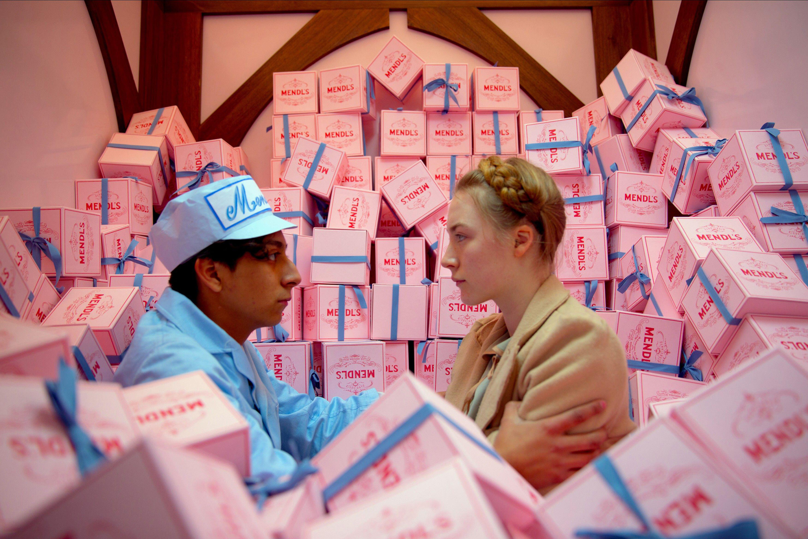 Ronan and Revolori from The Grand Budapest Hotel, surrounded by pink "Mendl's" boxes.