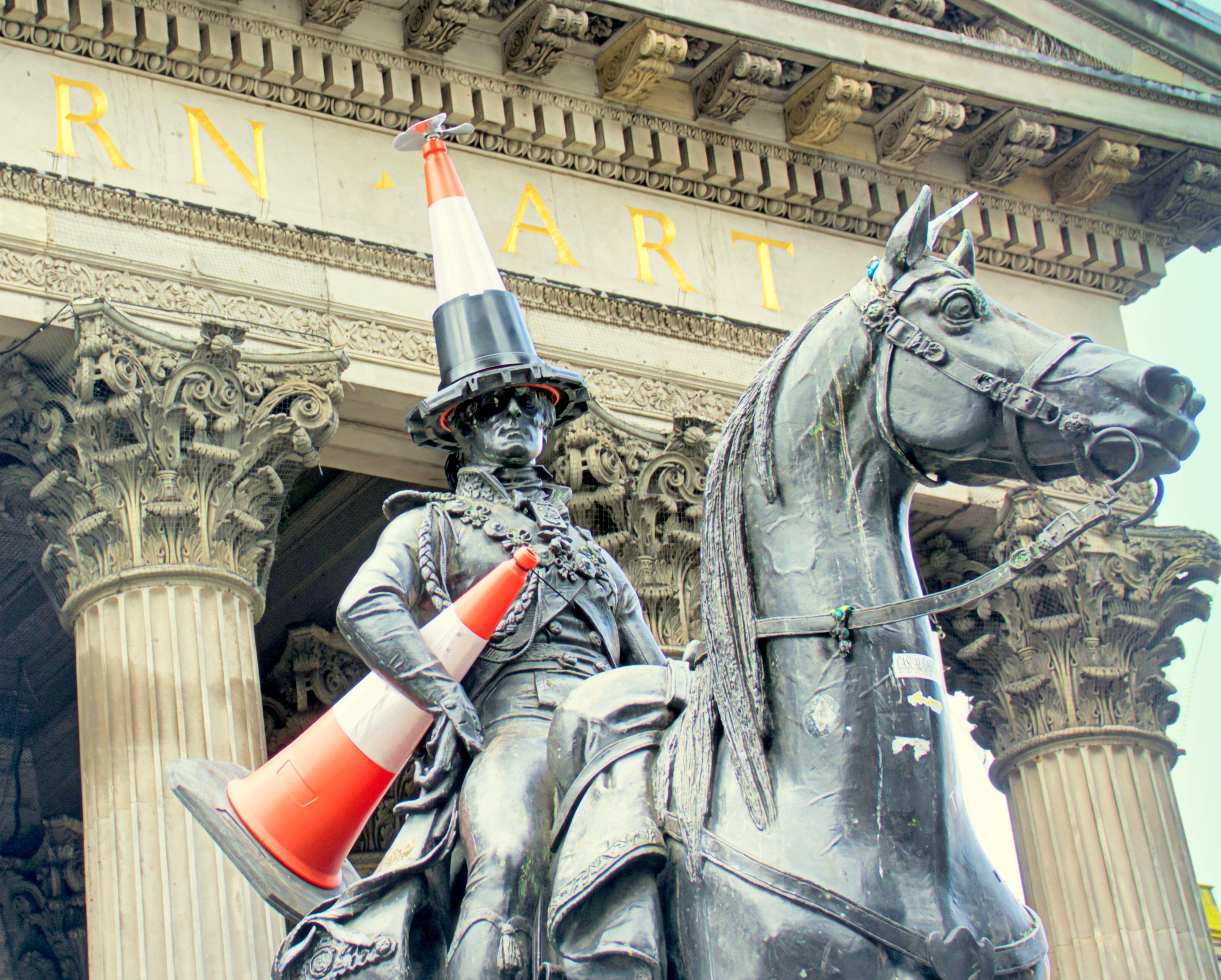 Equestrian statue of the Duke of Wellington with a traffic cone on his head, another cone on his arm, and a propeller head cone.