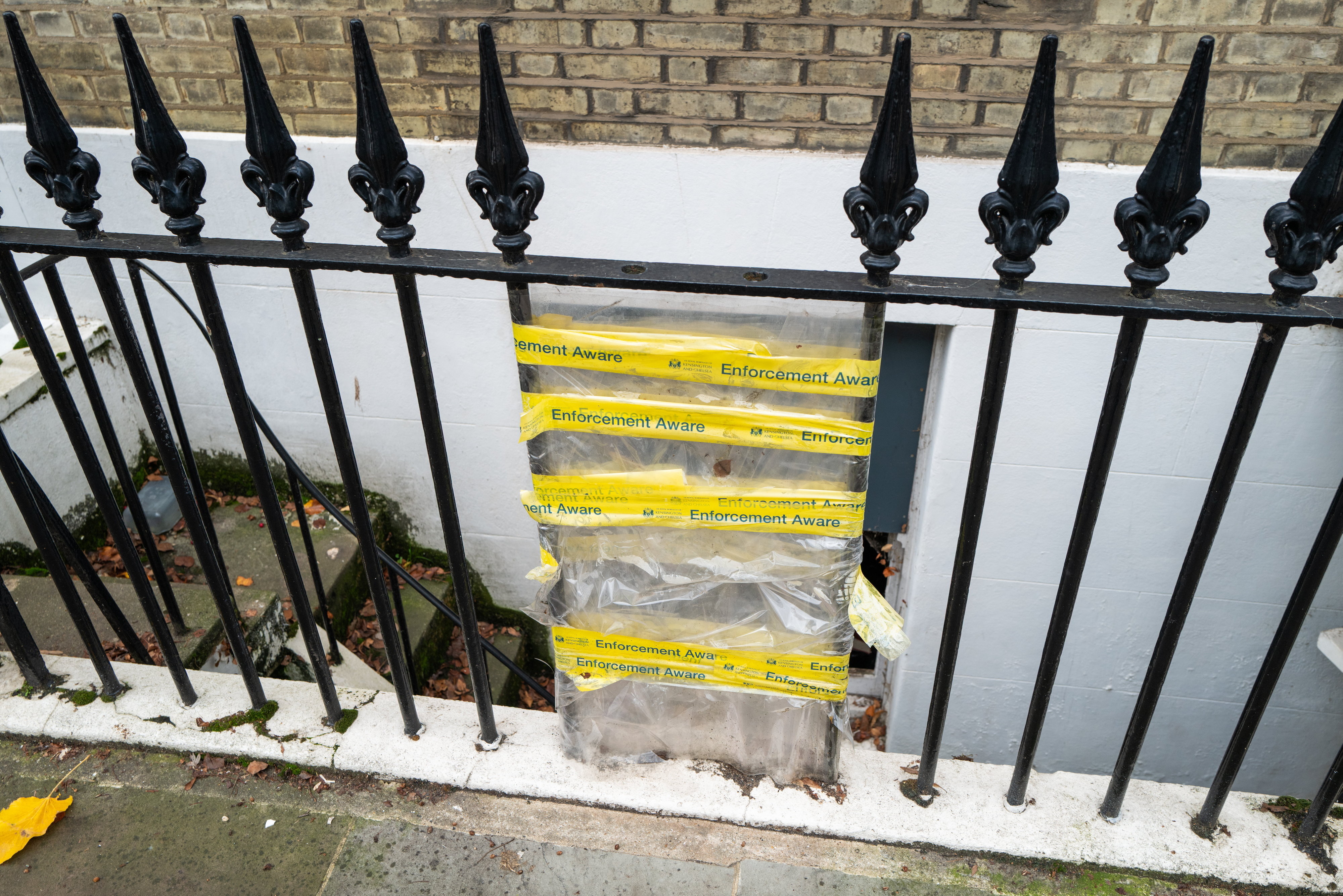 Black iron fence with "Enforcement Aware" tape from Kensington and Chelsea council.