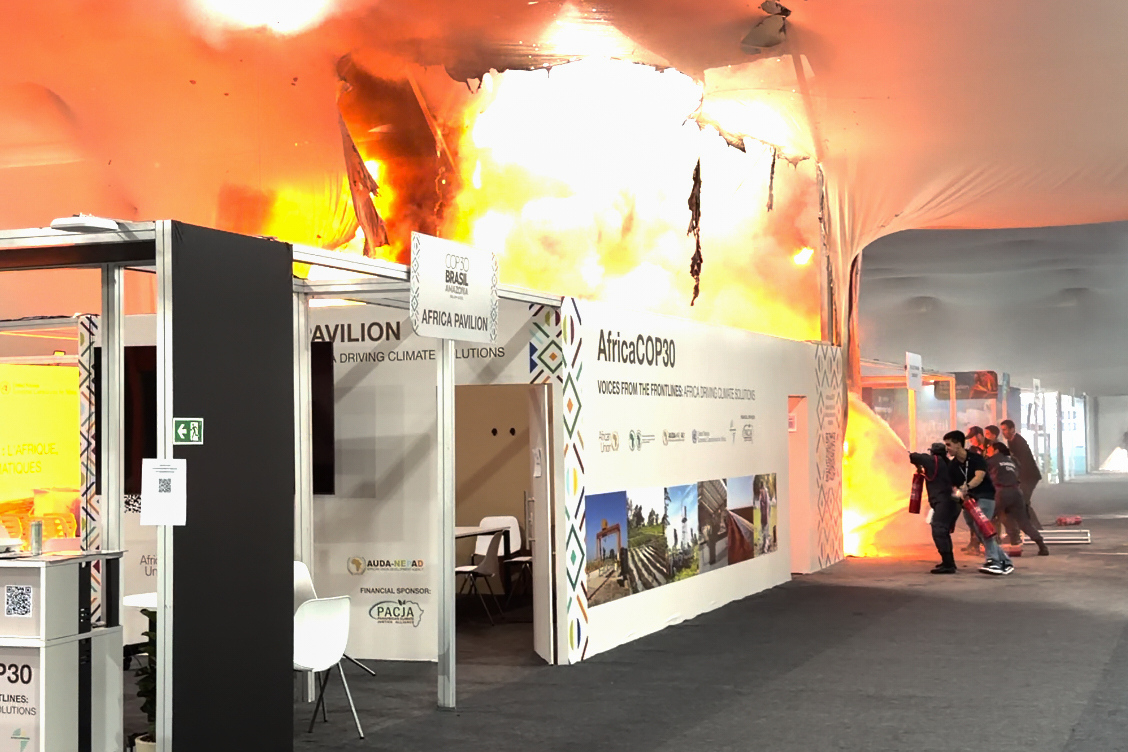 Flames engulf the Africa Pavilion at the COP30 U.N. Climate Summit while people attempt to put out the fire with extinguishers.