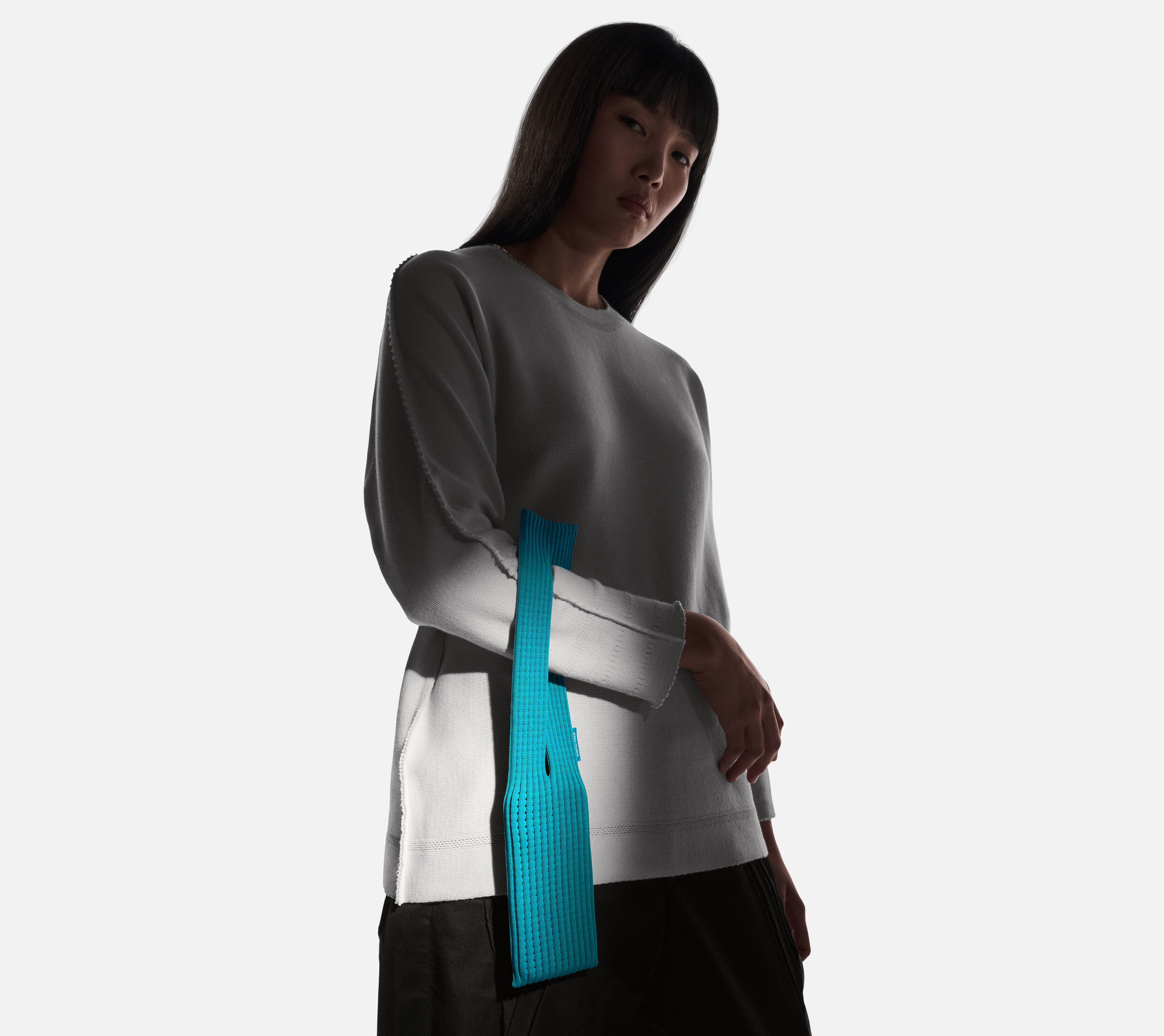 A person wearing a light grey top and black pants, with an iPhone Pocket in teal blue attached to their side.