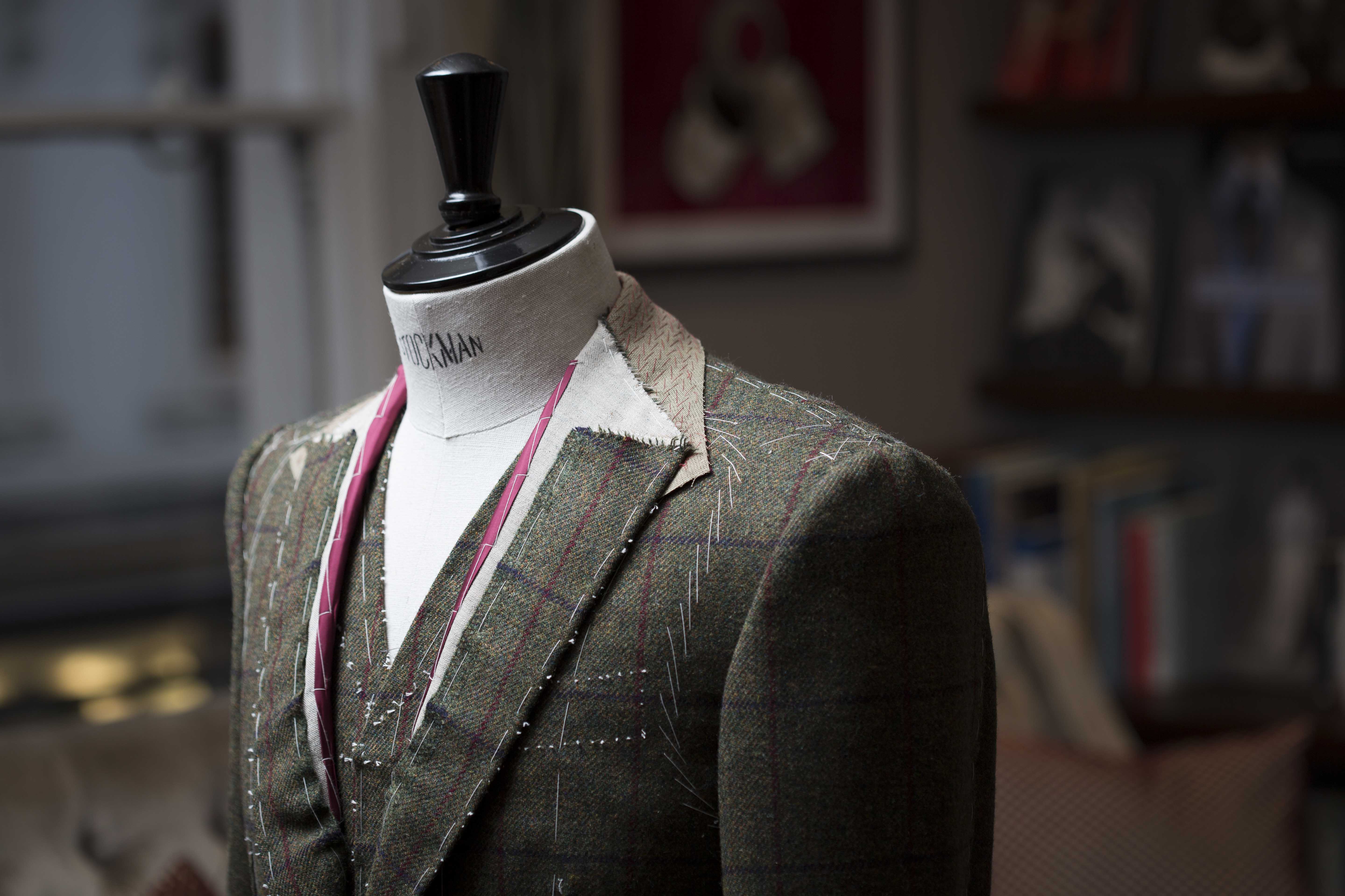 A green plaid jacket being tailored on a mannequin.