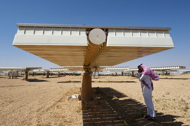 A man stands in the shade underneath a solar panel at a plant in Uyayna, Saudi Arabia, in 2018.