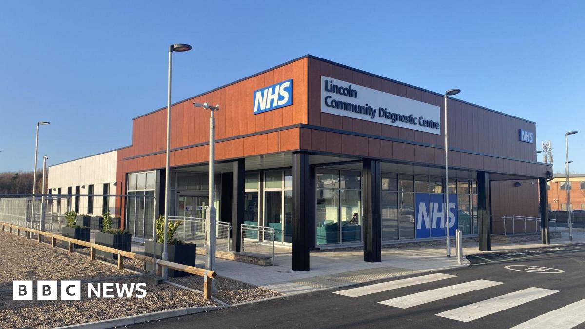 A modern building with open windows on the bottom with a brown upper floor exterior and the words NHS and Lincoln Community Diagnostic Centre written on it.