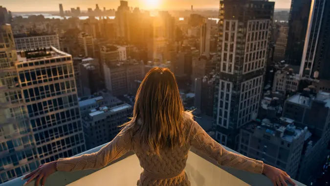 Rich woman enjoying the sunset standing on the balcony at luxury apartments in New York City.