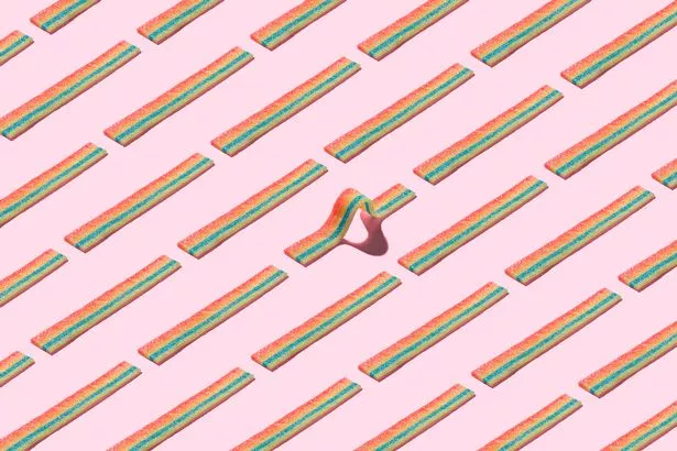 A Curved Rainbow Striped Candy Standing Out Form the Crowd on Solid Pink Colored Background.