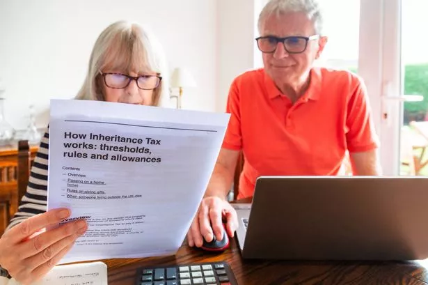 A senior married couple in their 70s study inheritance tax documents sitting down in their living room at home. The couple have serious, worried expressions as they study the information.