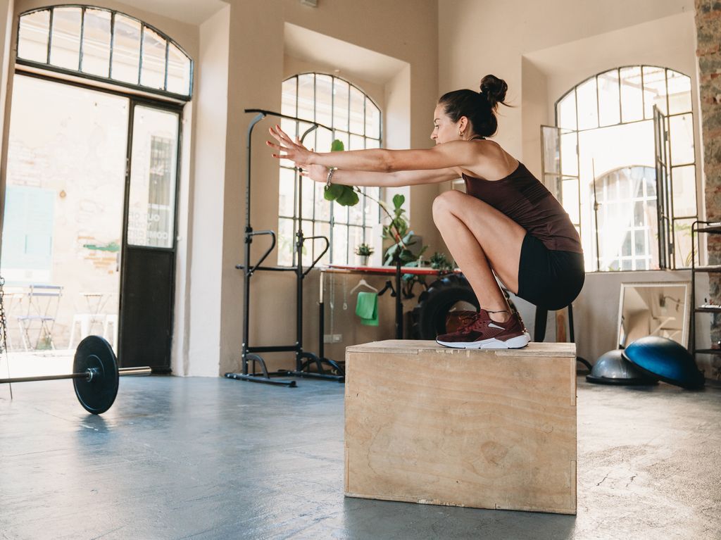 A young adult woman is training in the health club. She's jumping on a box.