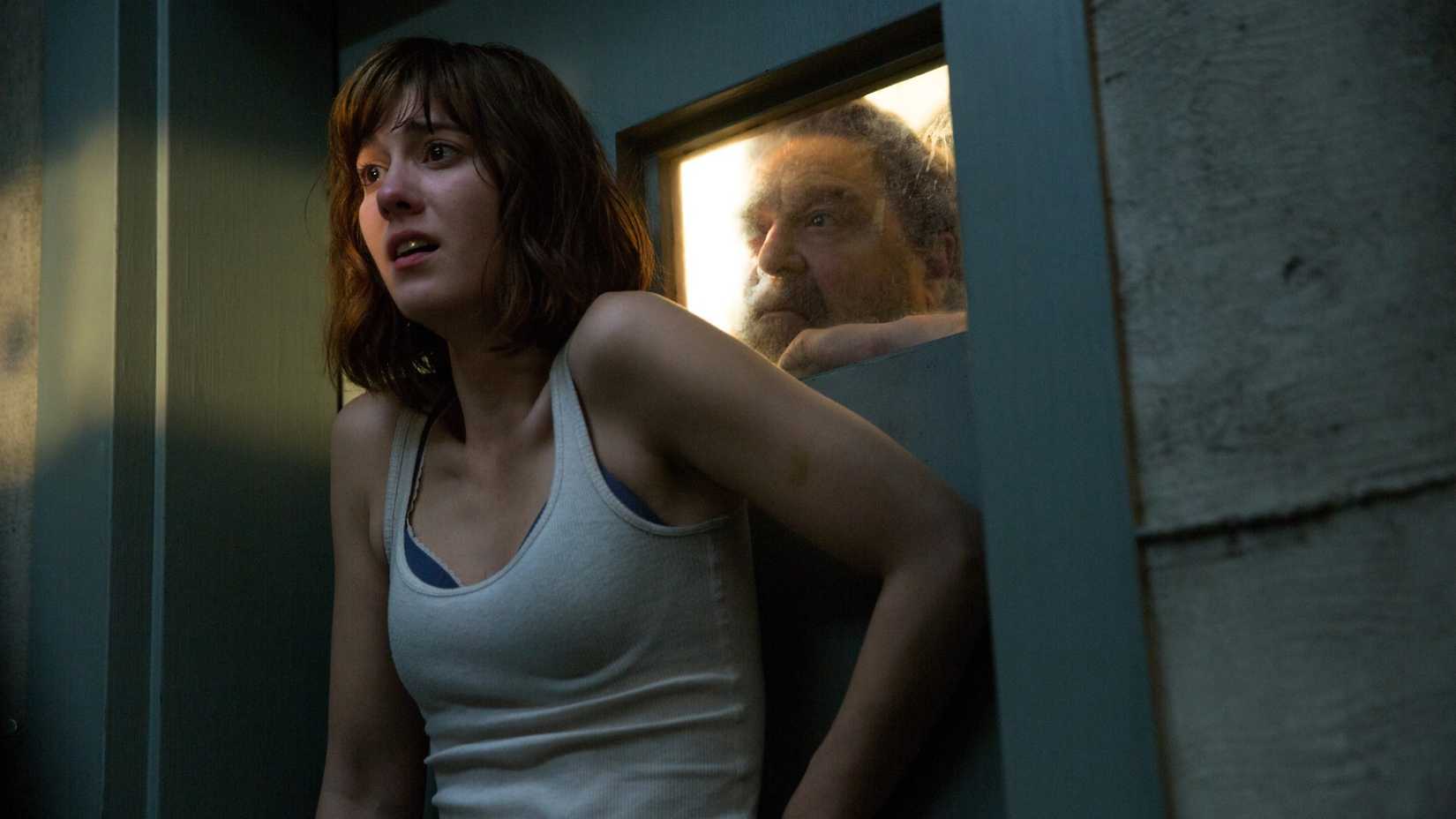 Mary Elizabeth Winstead cowers against a door while John Goodman looks through a window in10 Cloverfield Lane