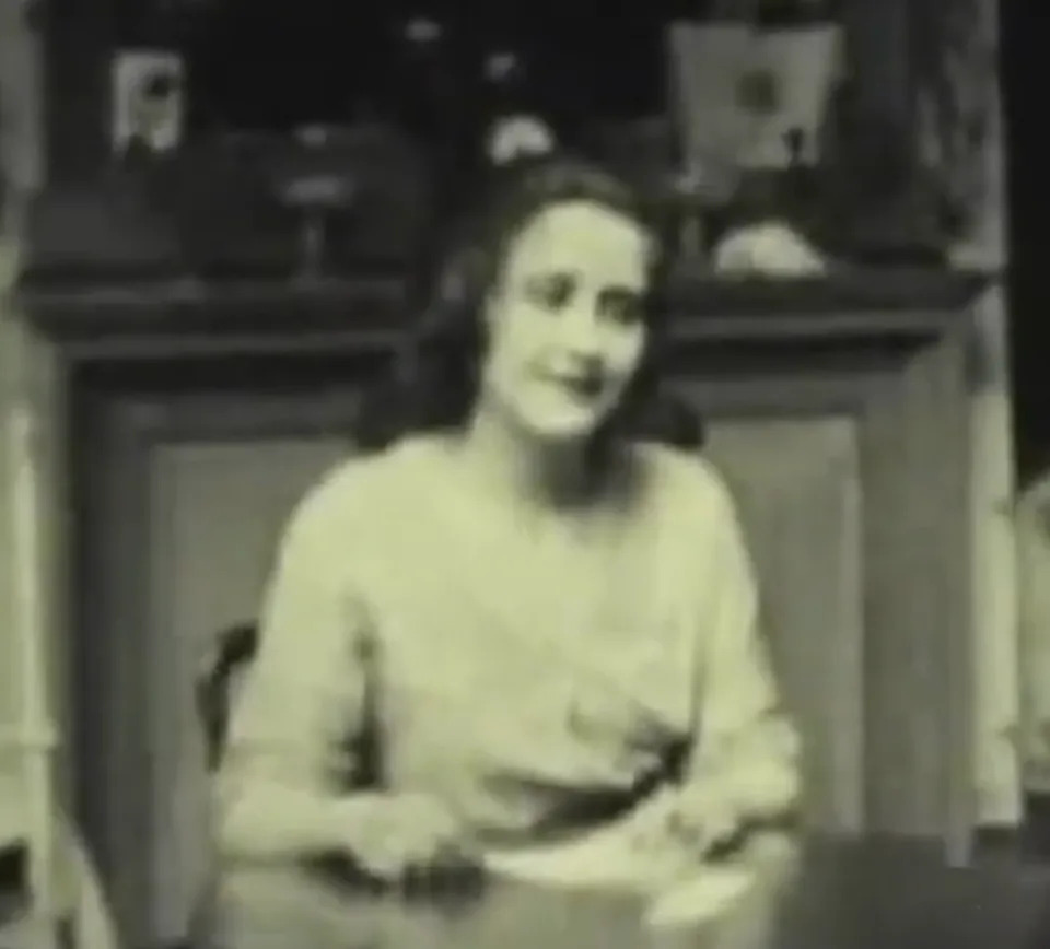 Clara Kimball Young as Trilby in vintage attire sits at a table, smiling gently, hypnotized