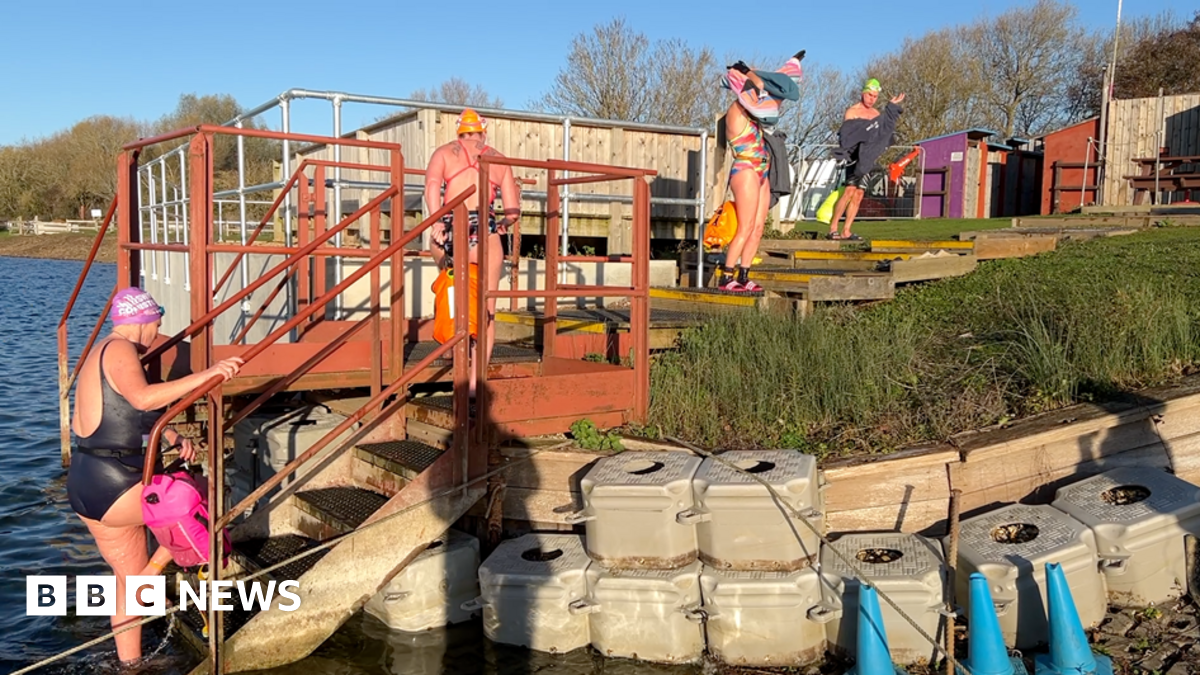 Four people getting in or out of the lake, with people drying themselves off or climbing out of it.