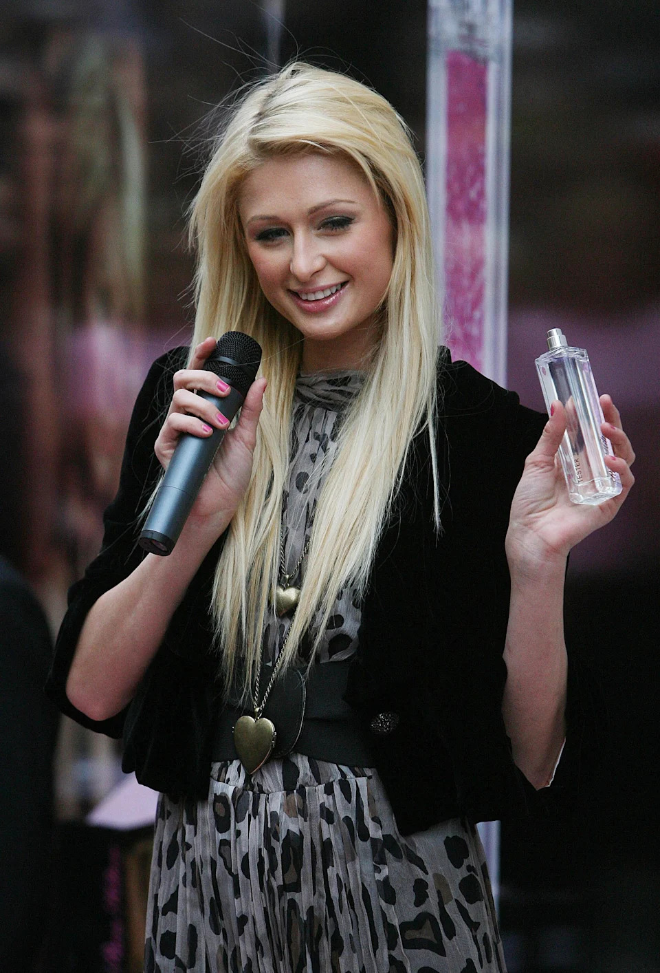 Paris Hilton holding a microphone and a perfume bottle, wearing a leopard print dress with a jacket