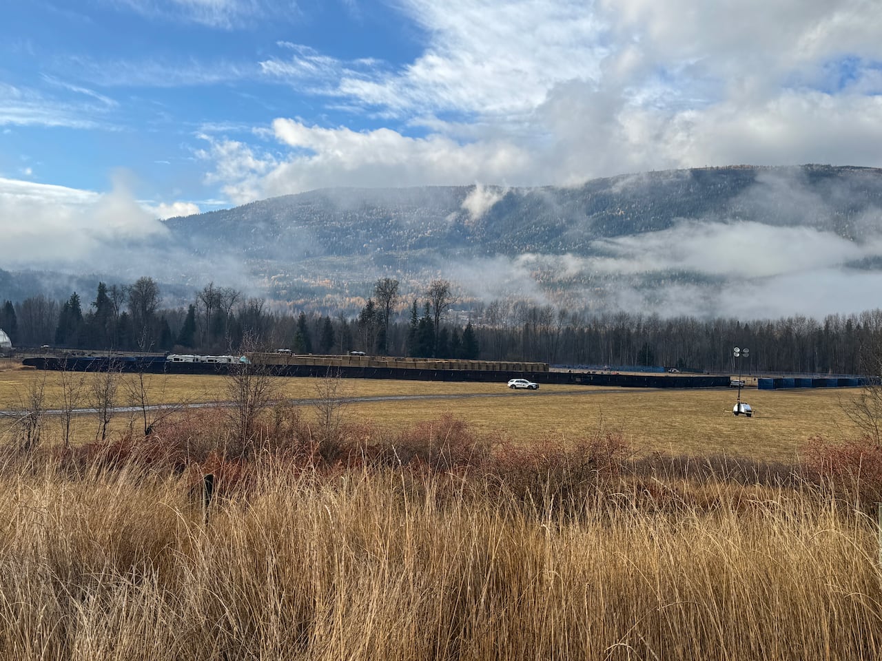 Bails of hay are stacked inside a large rectangular are lined with black fences.