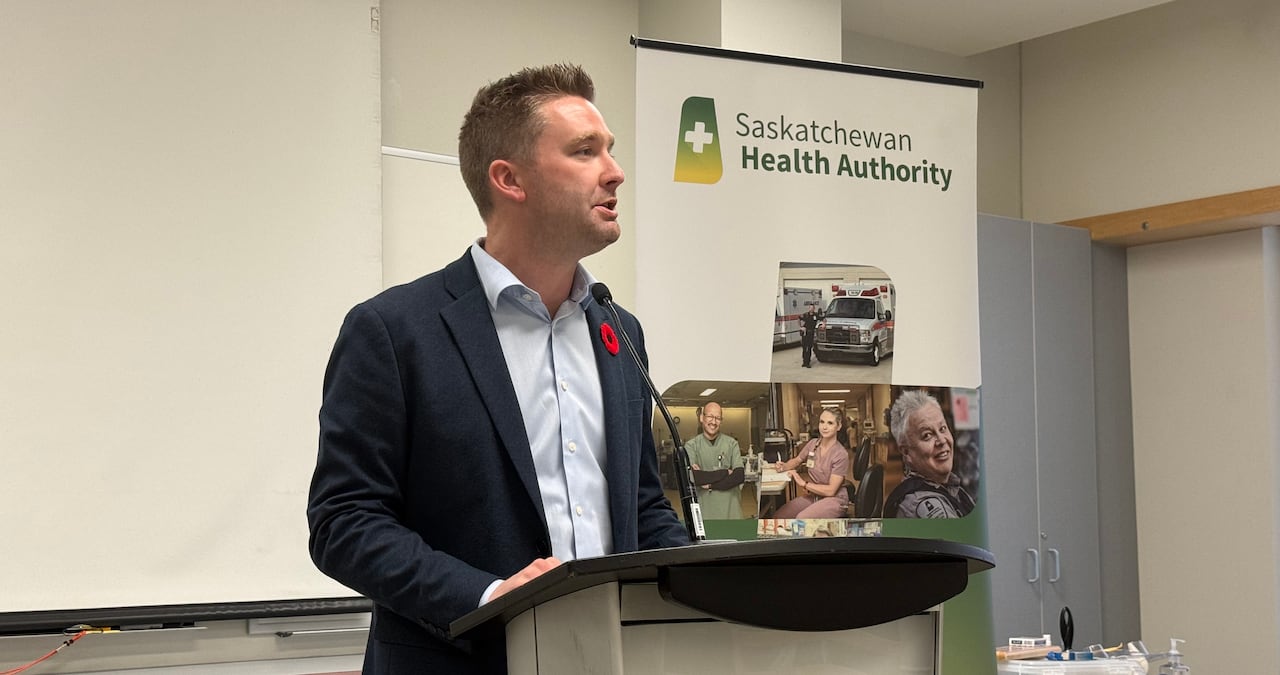 A man in a blue suit stands at a podium speaking into a microphone.
