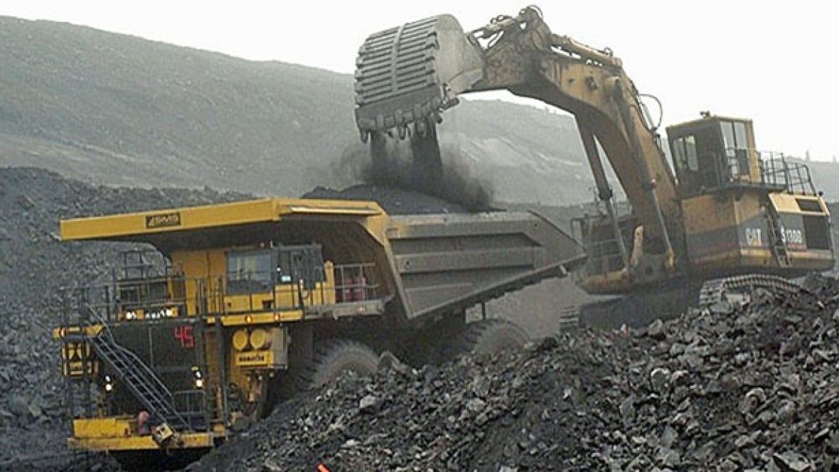 A backhoe fills a large truck with dark material.