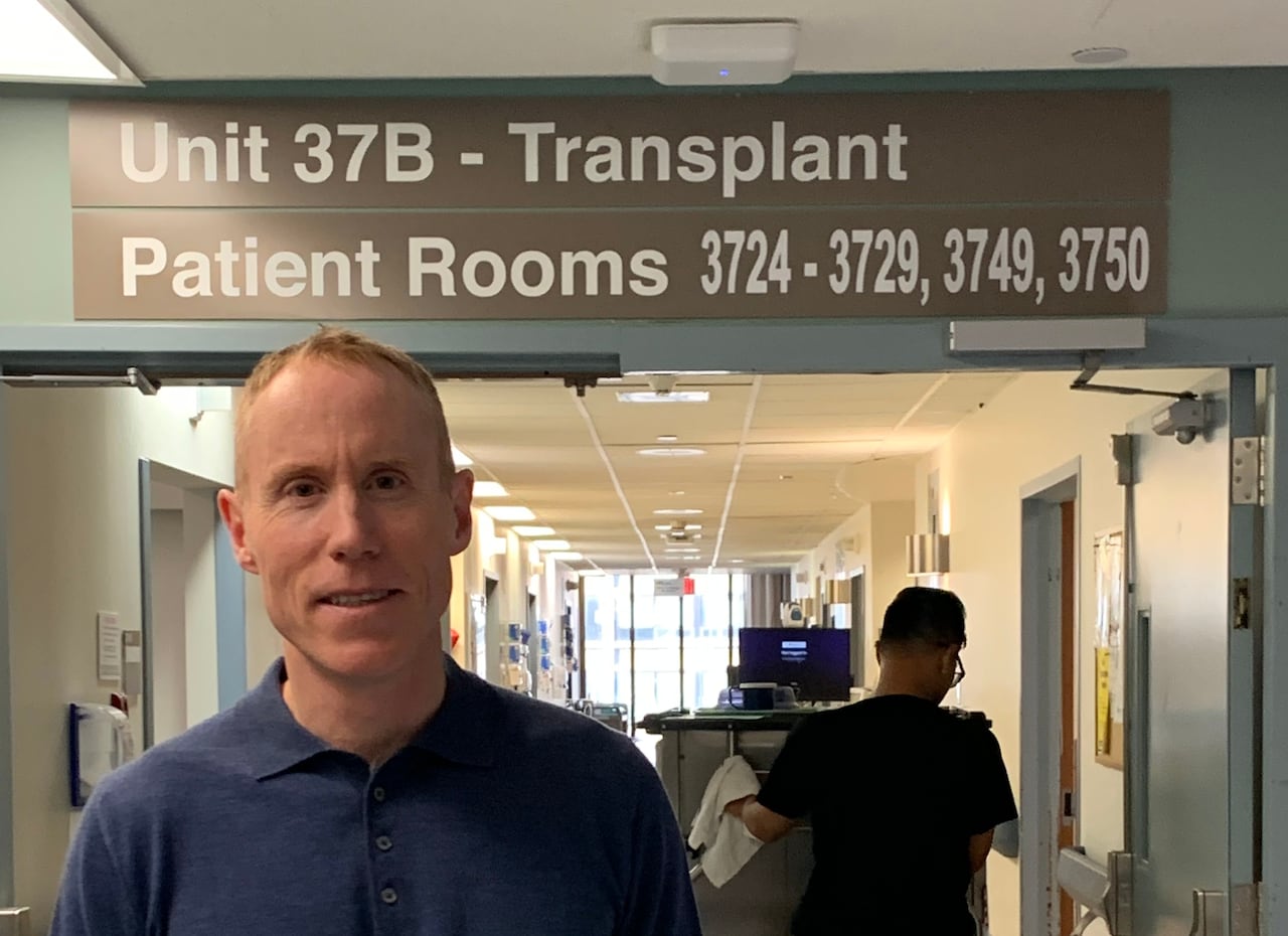 A man stands in front of a sign that says "transplant" in a hospital in Calgary.