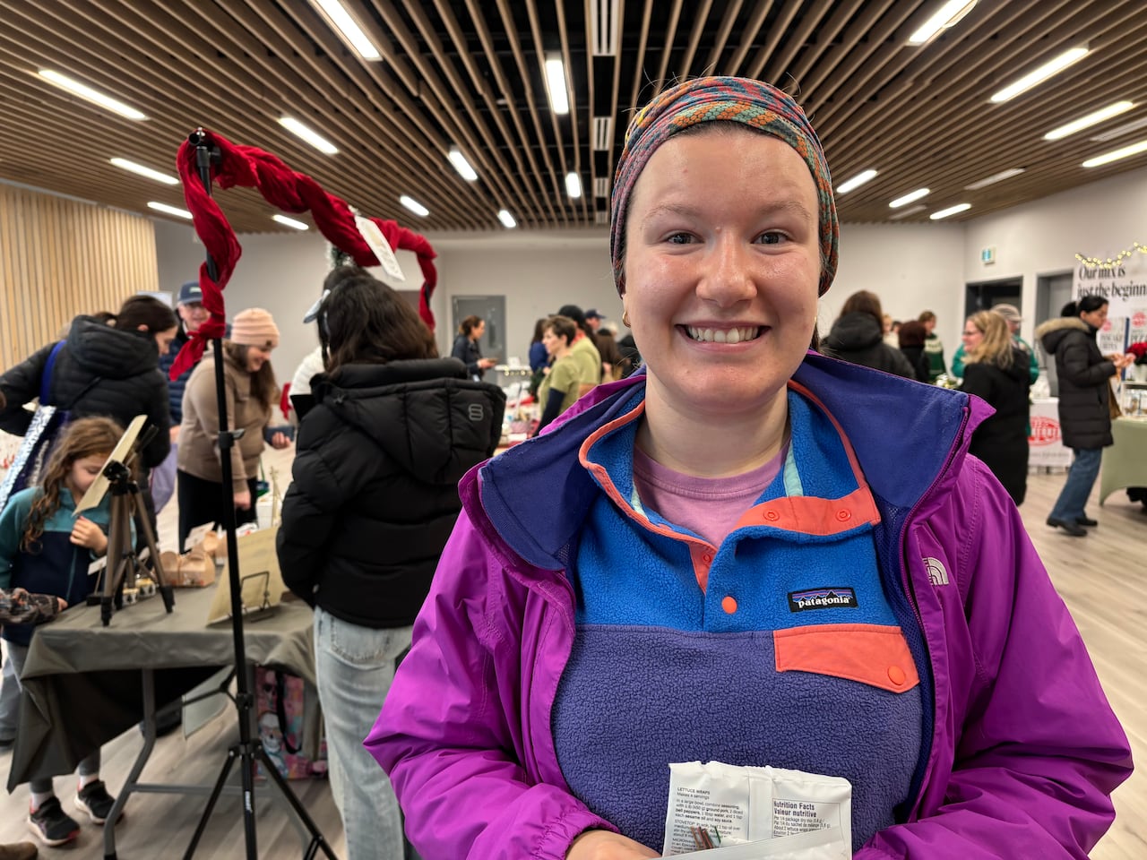 A woman wearing a Patagonia sweater and magenta North Face jacket stands in front of a hall of vendors and people